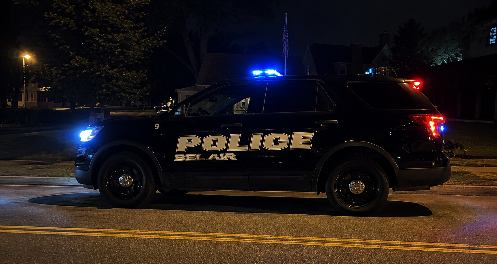 Belair police SUV with flashing blue lights parked on a dark street at night.