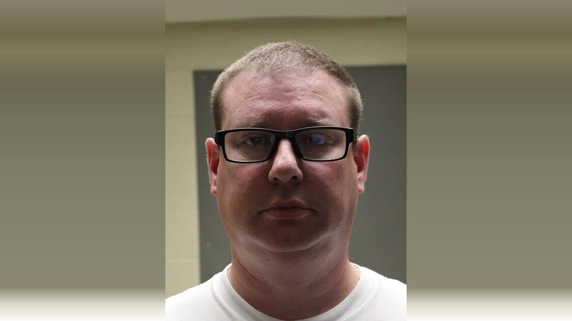 Portrait of a man wearing black glasses against a muted indoor background.