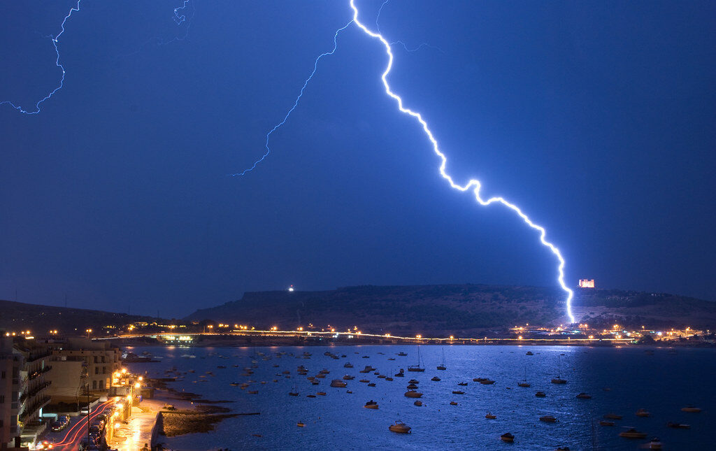 Lightning strikes over a coastal town and harbor at night