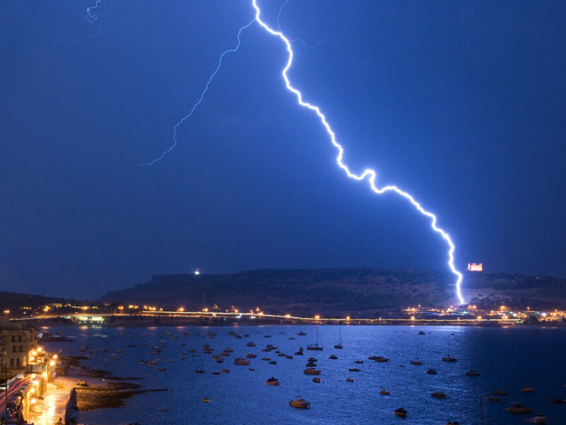 Lightning strikes over a coastal town and harbor at night