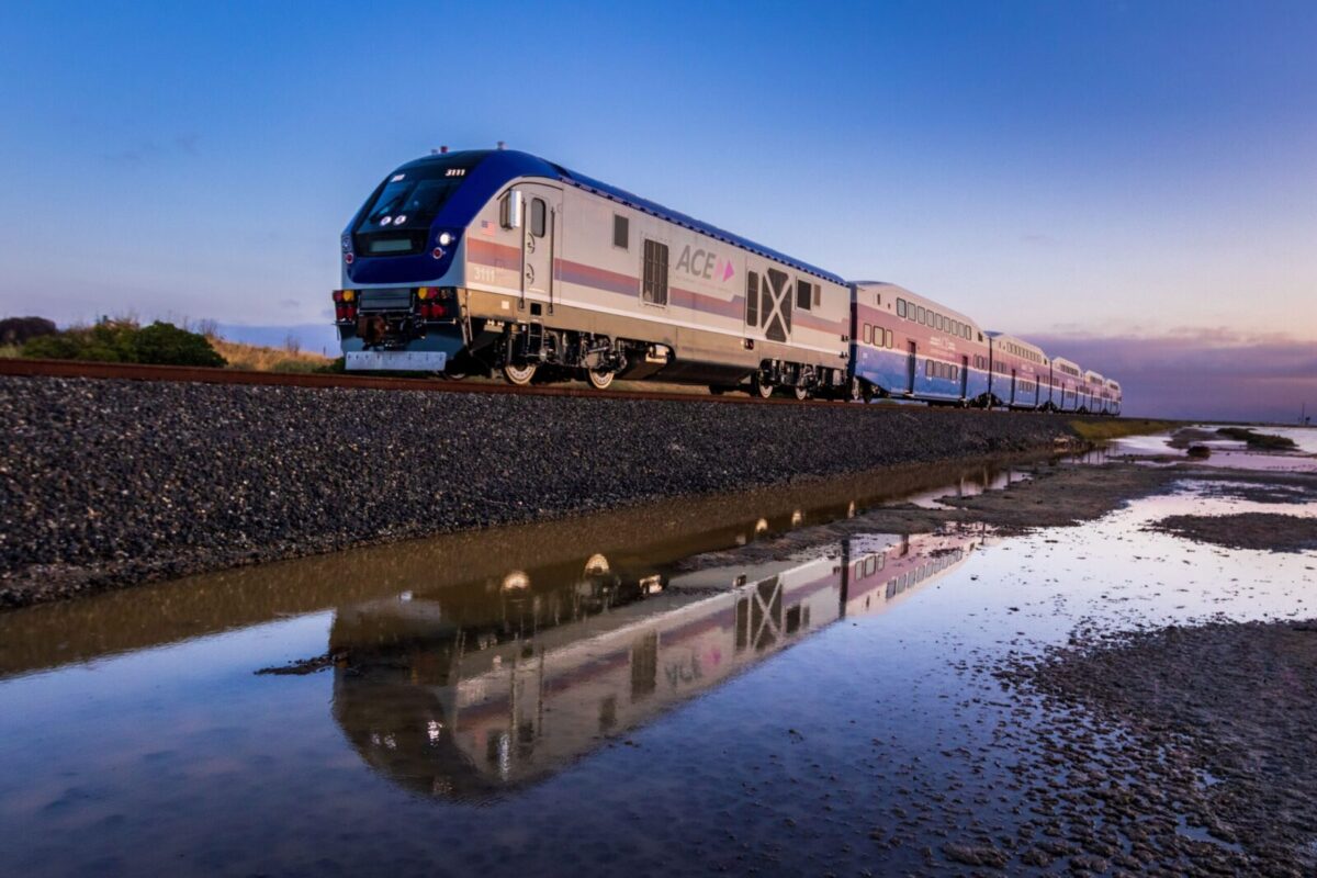 A high-speed train reflected in water at sunrise creates a serene transportation scene.