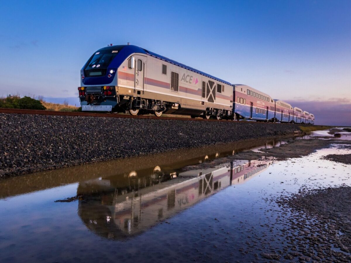A high-speed train reflected in water at sunrise creates a serene transportation scene.