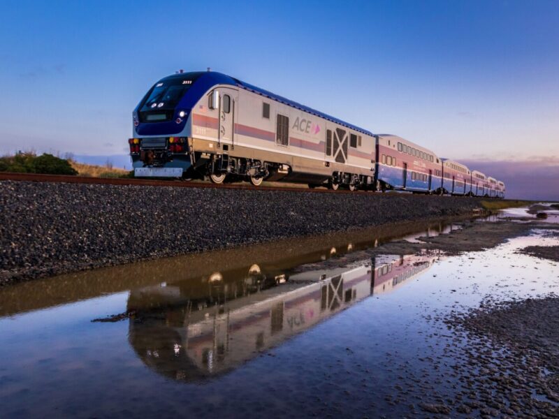 A high-speed train reflected in water at sunrise creates a serene transportation scene.
