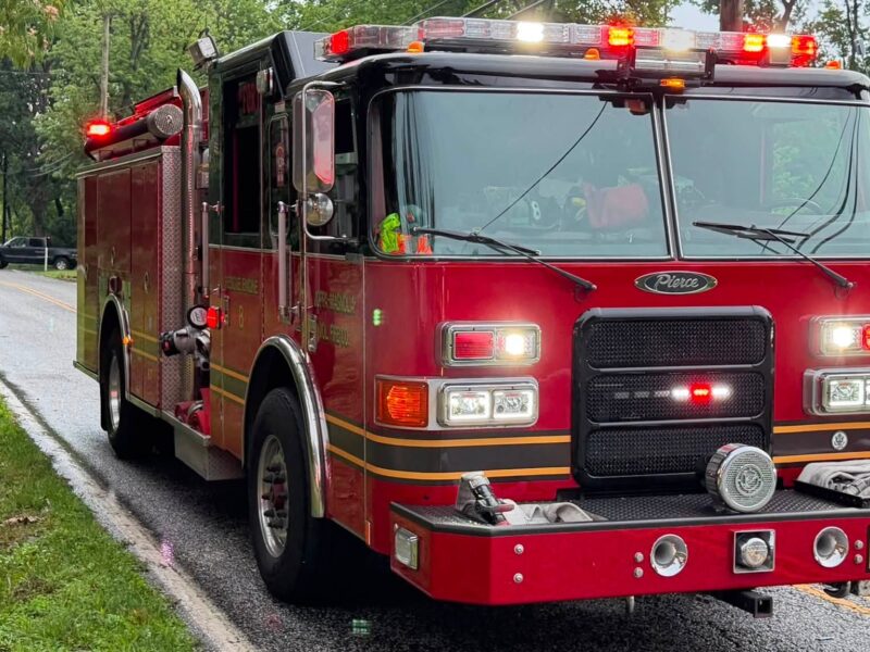 Red fire truck parked on a wet roadside with lights flashing in the rain.