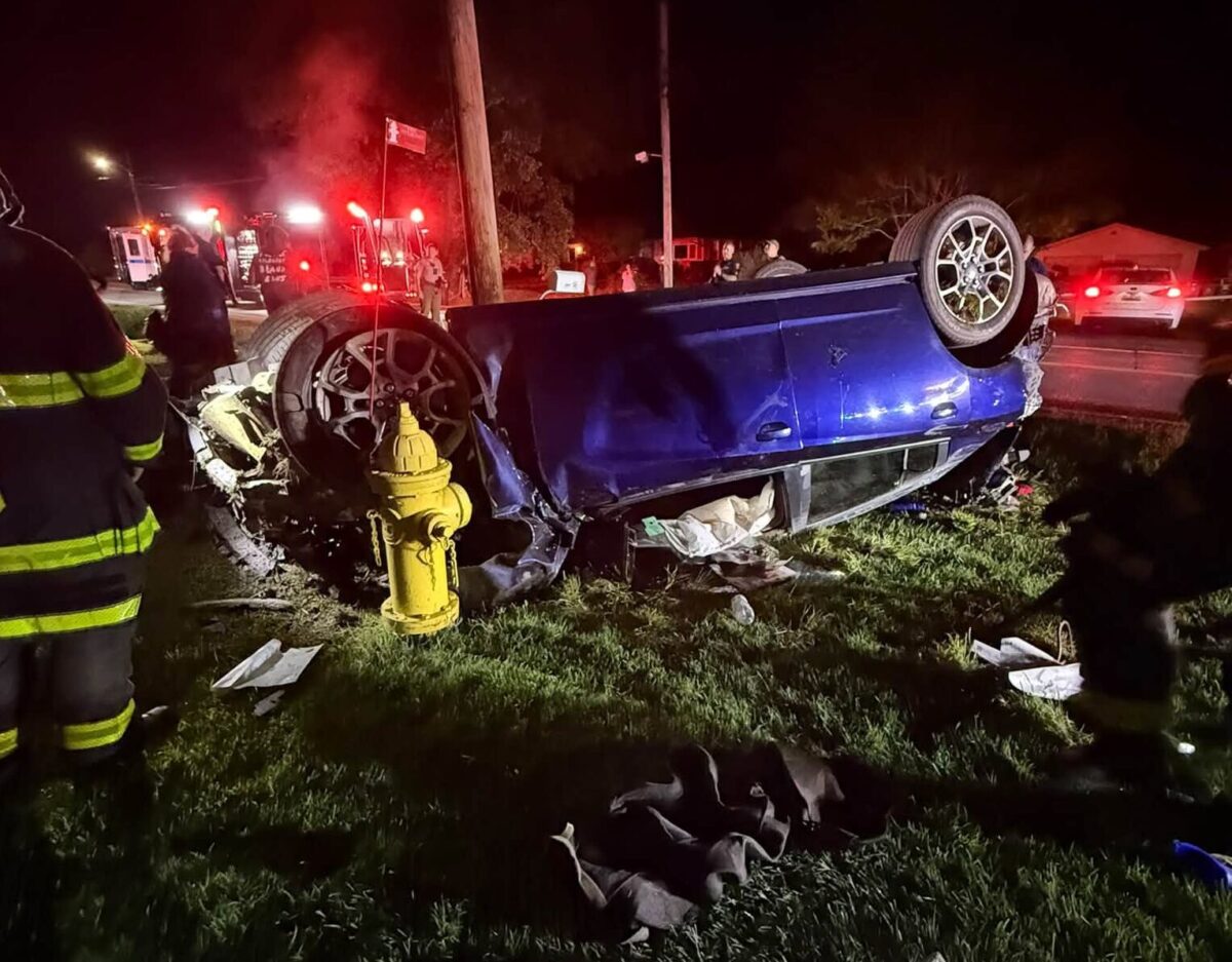 Overturned blue car beside a yellow fire hydrant at a nighttime crash scene with emergency lights.