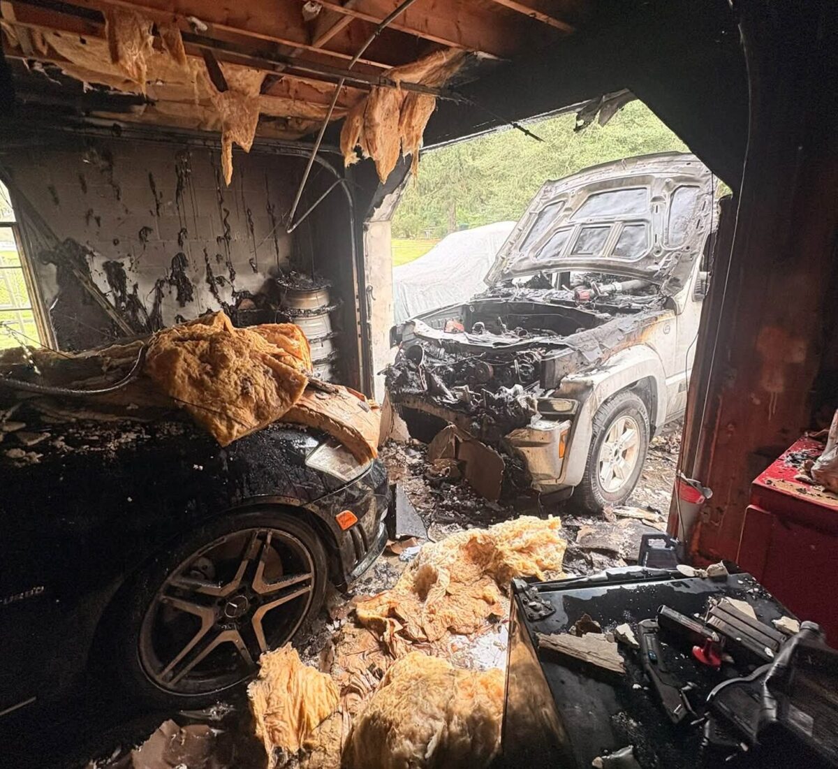 Burned vehicles sit in a fire-damaged garage with charred walls and debris.