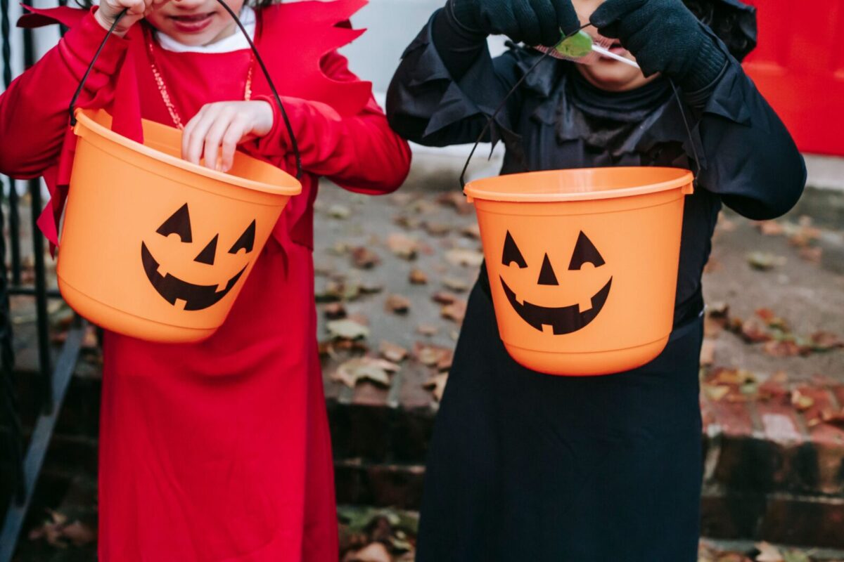 Crop anonymous children in Halloween costumes standing on stairs and holding buckets while choosing sweets