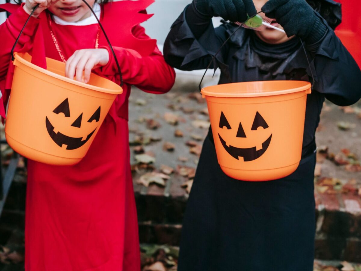 Crop anonymous children in Halloween costumes standing on stairs and holding buckets while choosing sweets